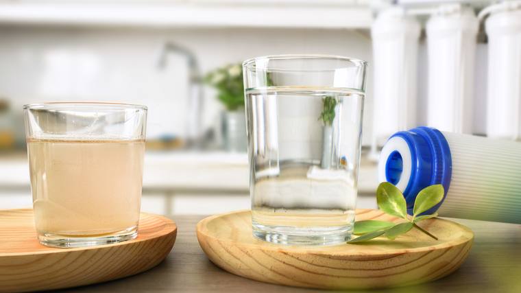 A glass of untreated water beside a glass of clear filtered water in a kitchen